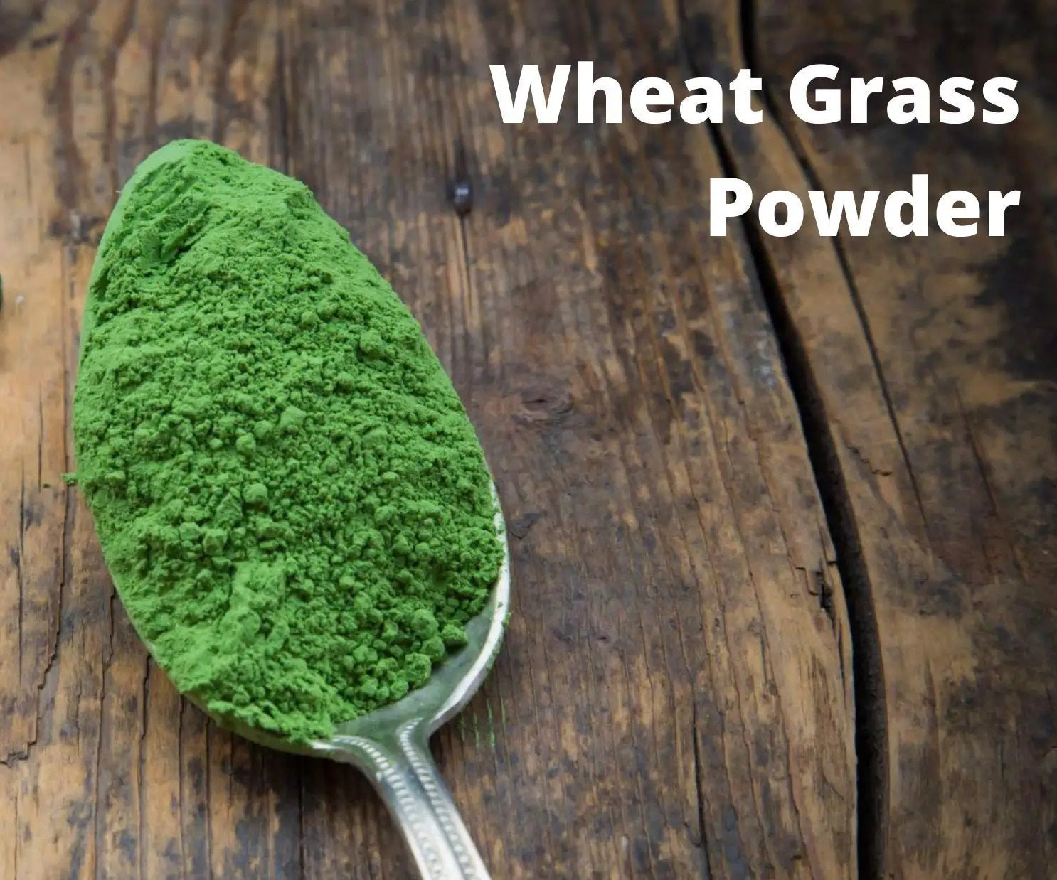 Spoonful of wheat grass powder on a wooden surface with text 'Wheat Grass Powder'.