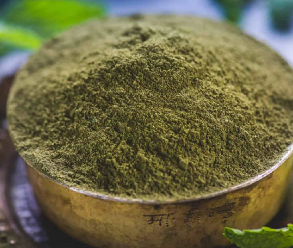 Close-up of a bowl filled with green powder, likely matcha, with a blurred natural background.